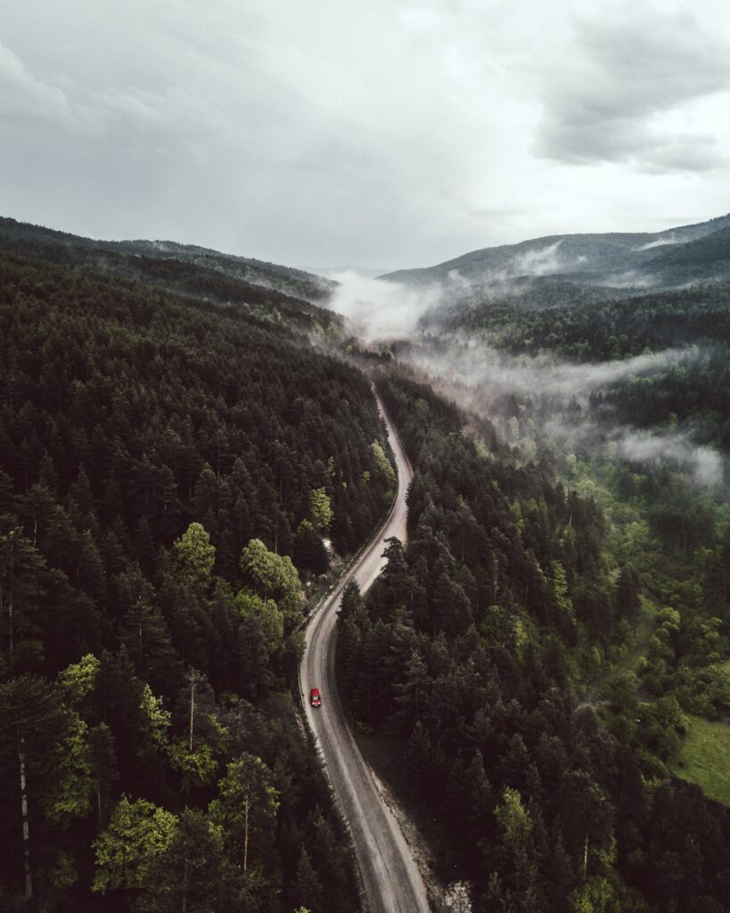 Aerial view of winding forest road with red car misty hills and distant mountains landscape wallpaper