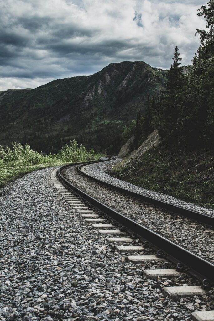 Winding railway track through green mountains under dramatic cloudy sky scenic nature wallpaper