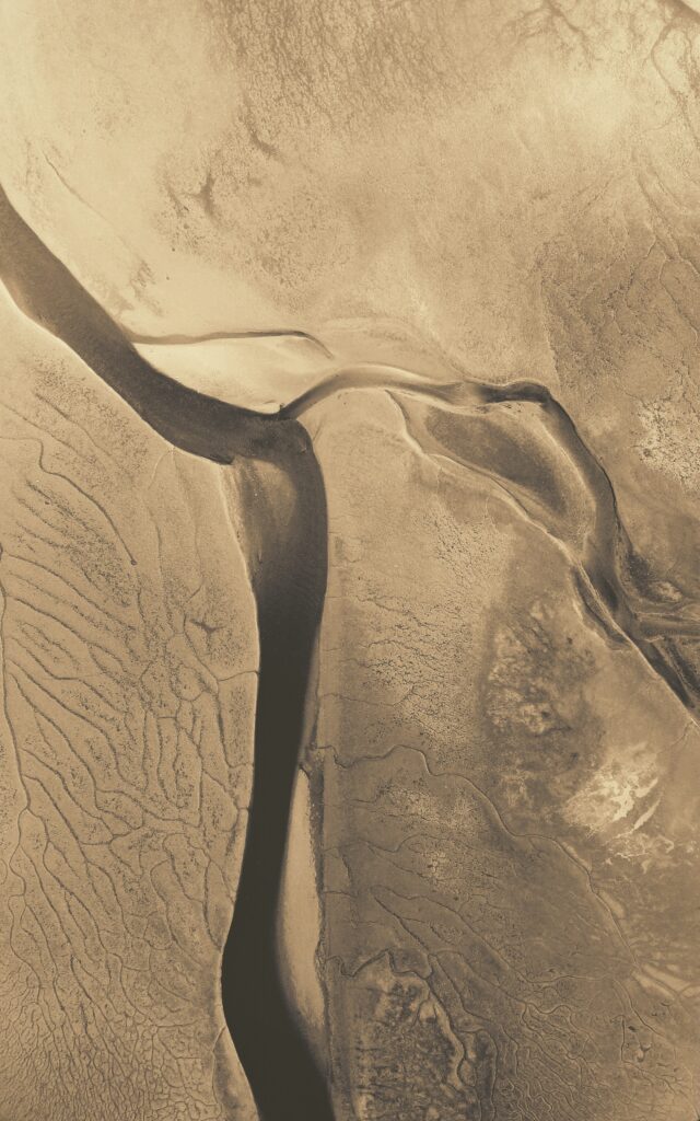 Aerial view of winding river through sandy terrain with earthy beige and brown textures Wallpaper