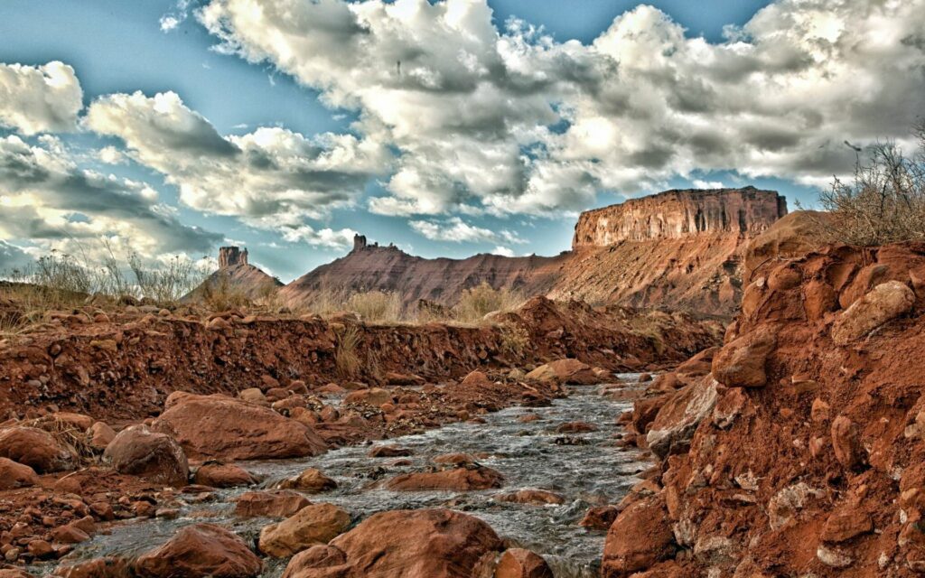 Winding river through red rocky terrain with rugged mountains and textured cloudy sky wallpaper background