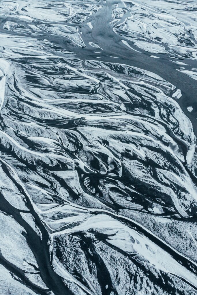 Aerial view of winding river through snowy winter landscape contrasting icy white and dark water Wallpaper