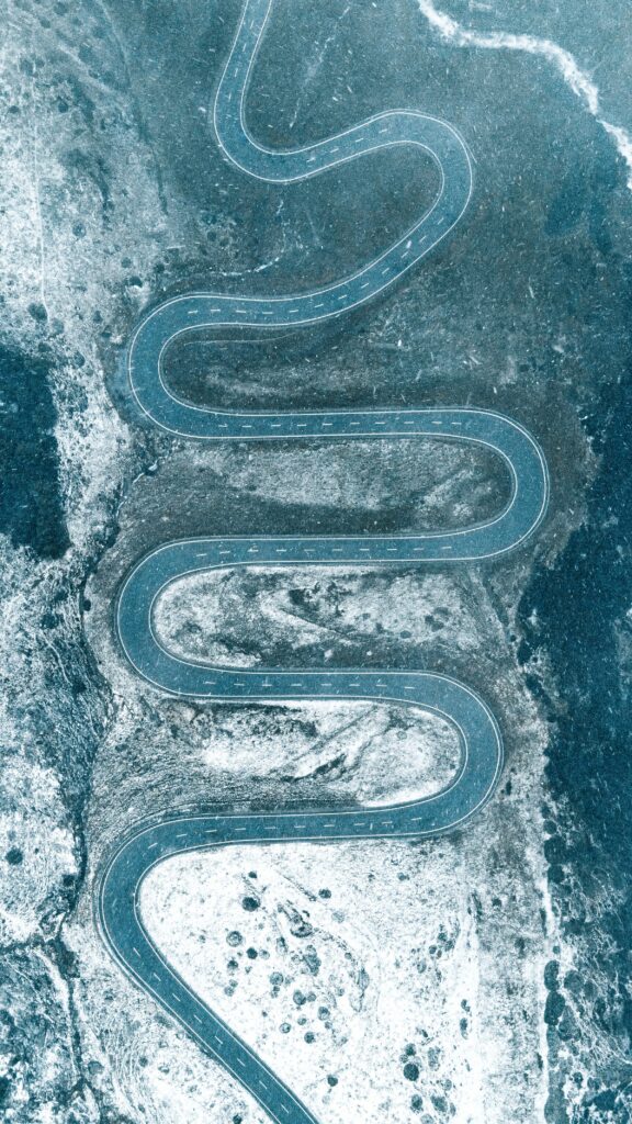 Aerial view of winding road through snowy landscape with blue winter tones wallpaper background
