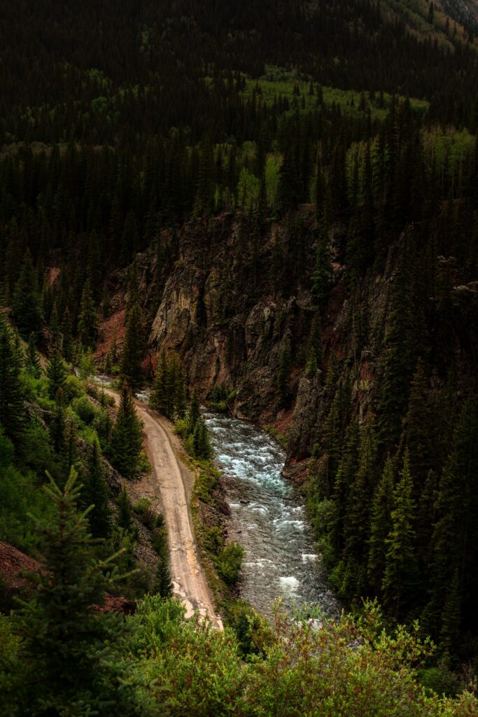 Aerial view of winding road beside clear river with cliffs and dense forest wallpaper background
