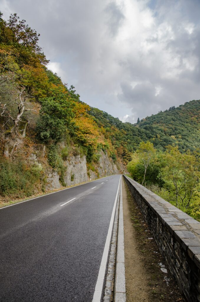 Winding road through green trees and rocky cliffs under dramatic cloudy sky wallpaper background