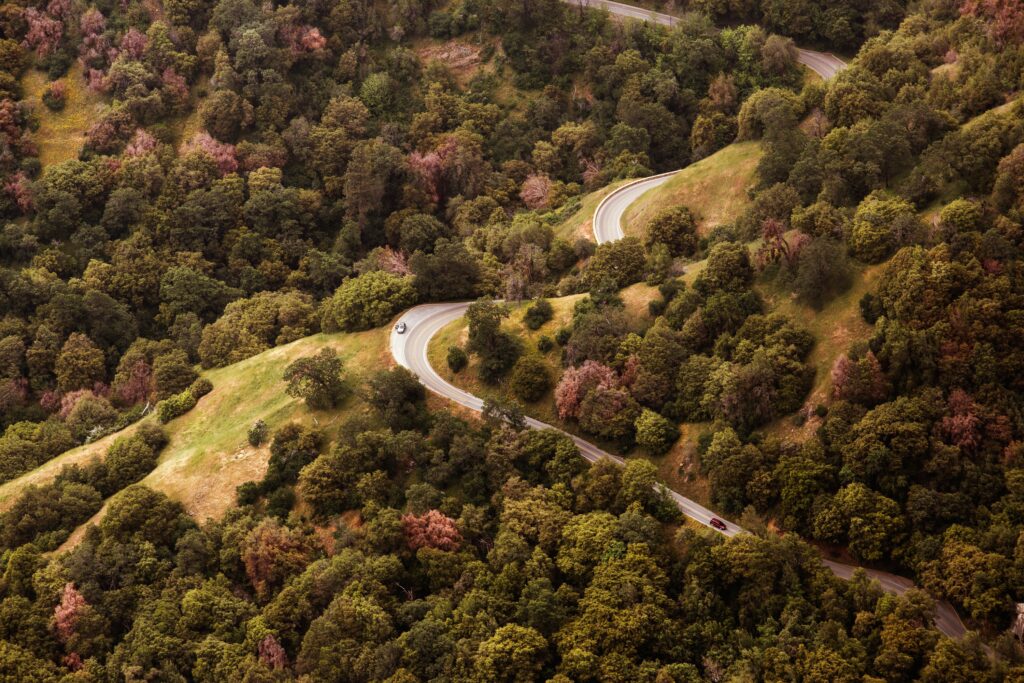 Aerial view of winding road through lush green hills with vibrant trees and traveling cars wallpaper