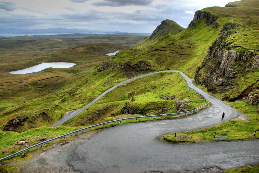 Winding road in lush Scottish mountains with solitary hiker under dramatic cloudy sky wallpaper