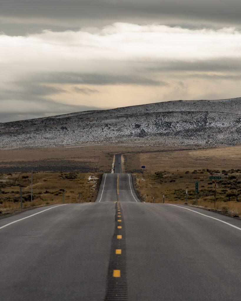 Long winding road through brown grassy hills and vast valley under dramatic cloudy sky wallpaper