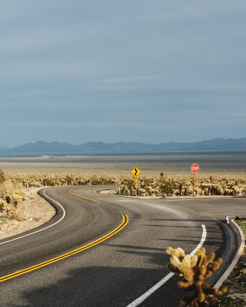 Winding road through open prairies hills dry grass desert shrubs serene sky distant mountains wallpaper