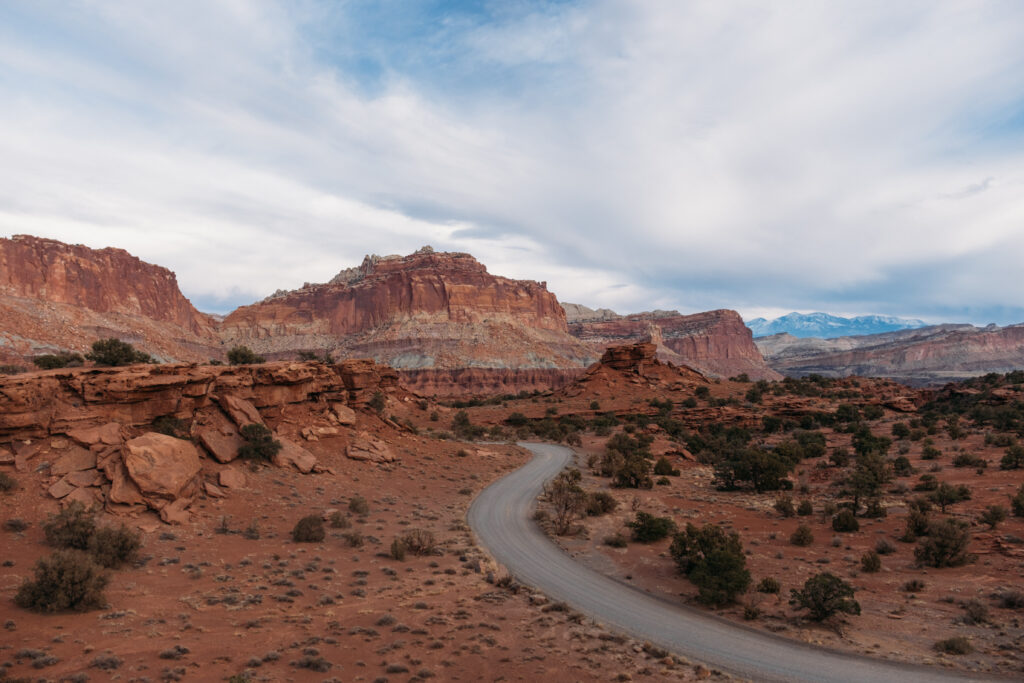 Winding road through red rock canyon with rugged cliffs and cloudy sky desert landscape wallpaper