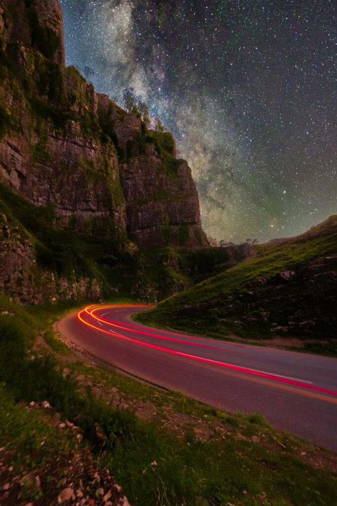 Winding road through rocky cliffs under starry sky with Milky Way and light trail motion effect Wallpaper