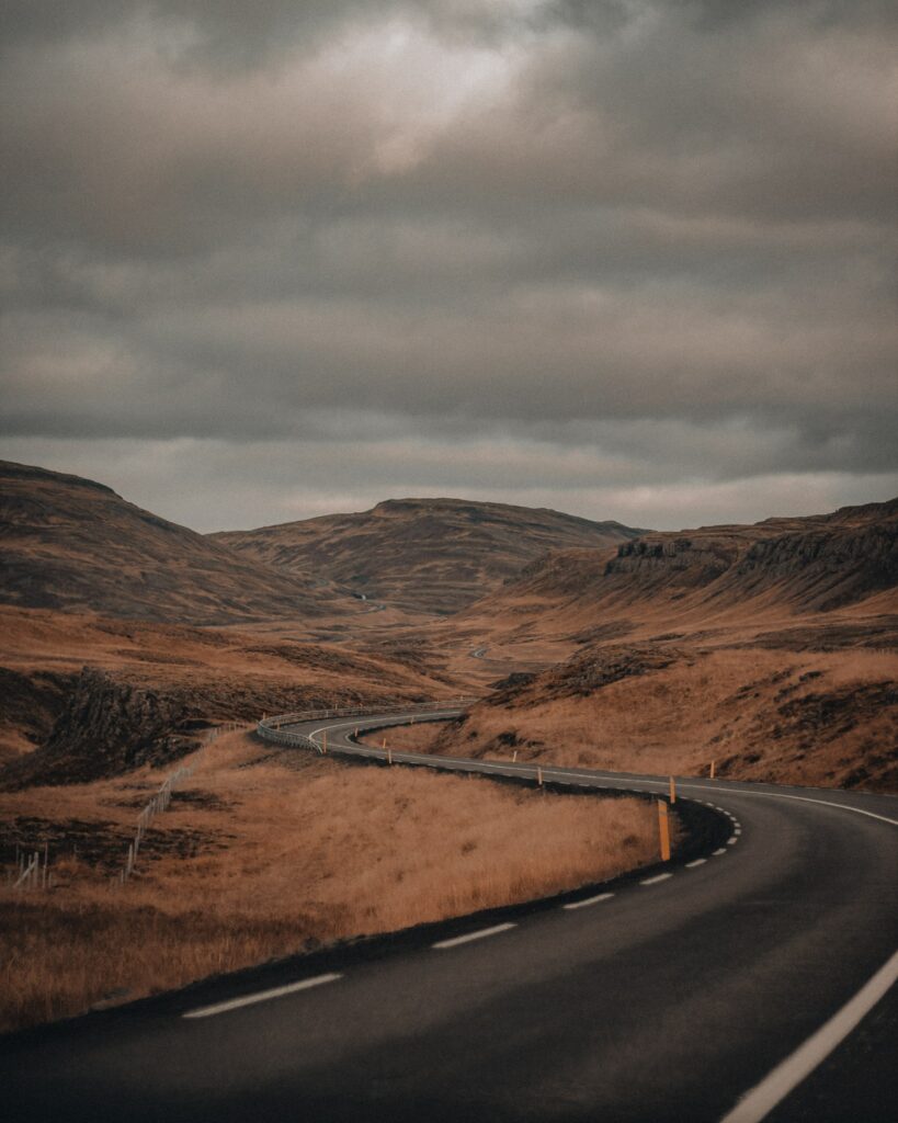 Winding road through rolling hills under cloudy sky with brown and gold landscape scenery wallpaper