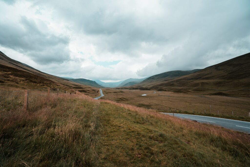 Winding road through rolling hills and grassy fields under dramatic cloudy sky scenic landscape Wallpaper