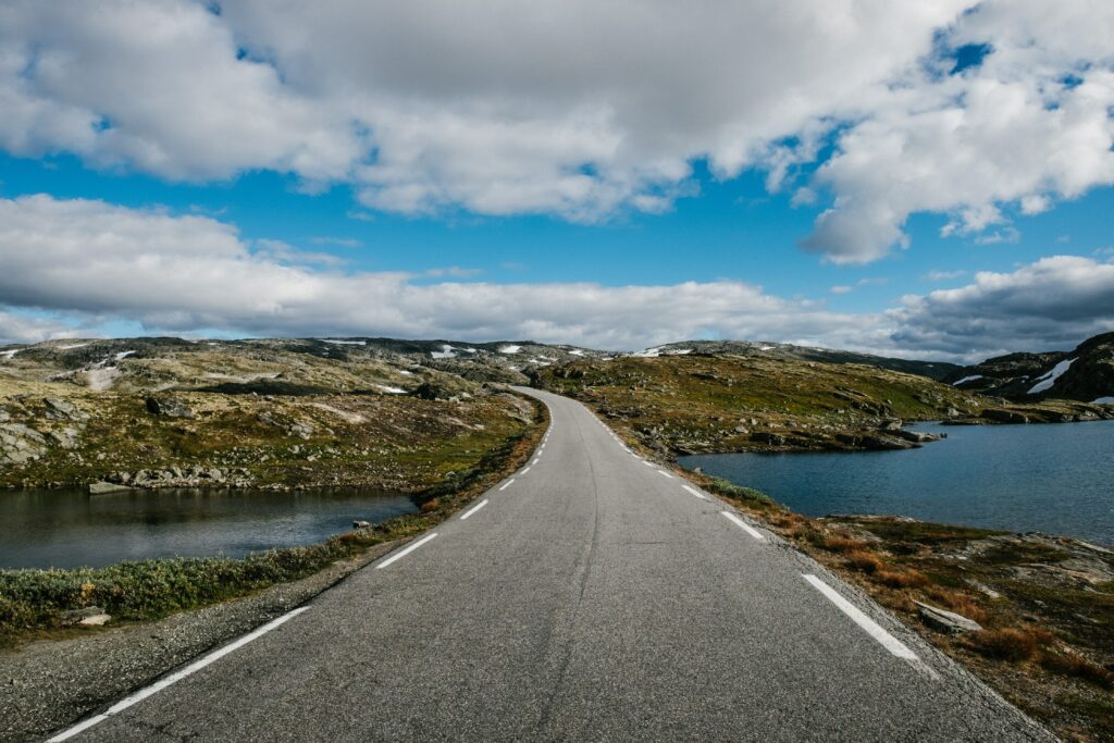 Winding road through rocky hills and calm water under vibrant blue sky with white clouds wallpaper
