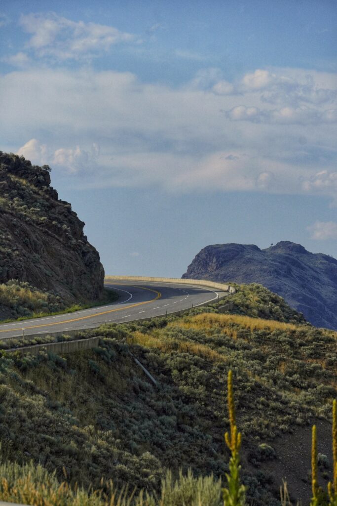 Winding road through rugged rocks and rolling hills under blue sky with scattered clouds wallpaper background