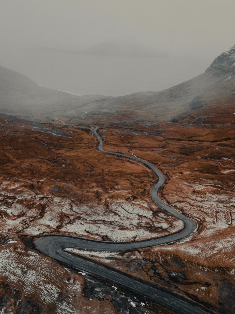 Winding road through snow dusted brown hills under foggy moody sky natural landscape wallpaper