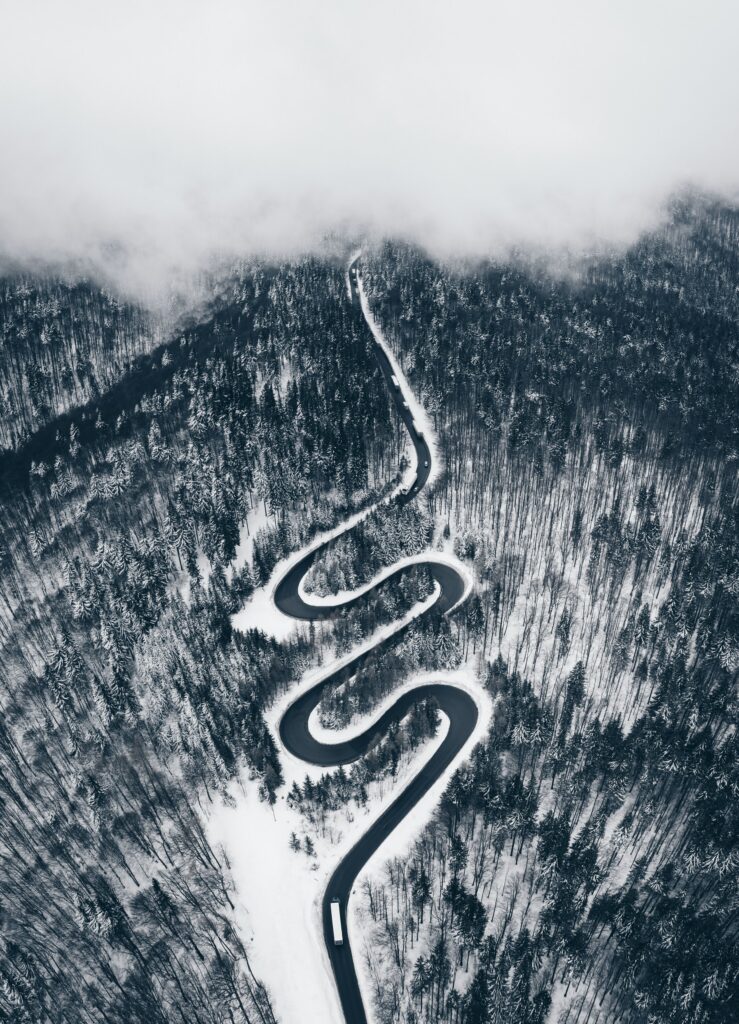 Aerial view of winding road through dense snow-covered forest with misty clouds winter landscape Wallpaper