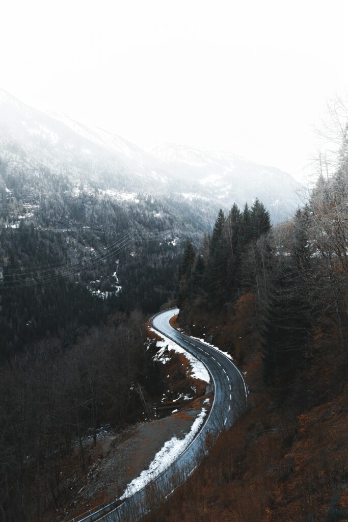 Winding road through snowy mountain forest with misty winter landscape wallpaper background