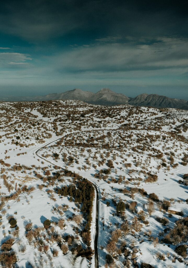 Aerial view of winding road through snowy landscape with trees and mountains under moody sky Wallpaper