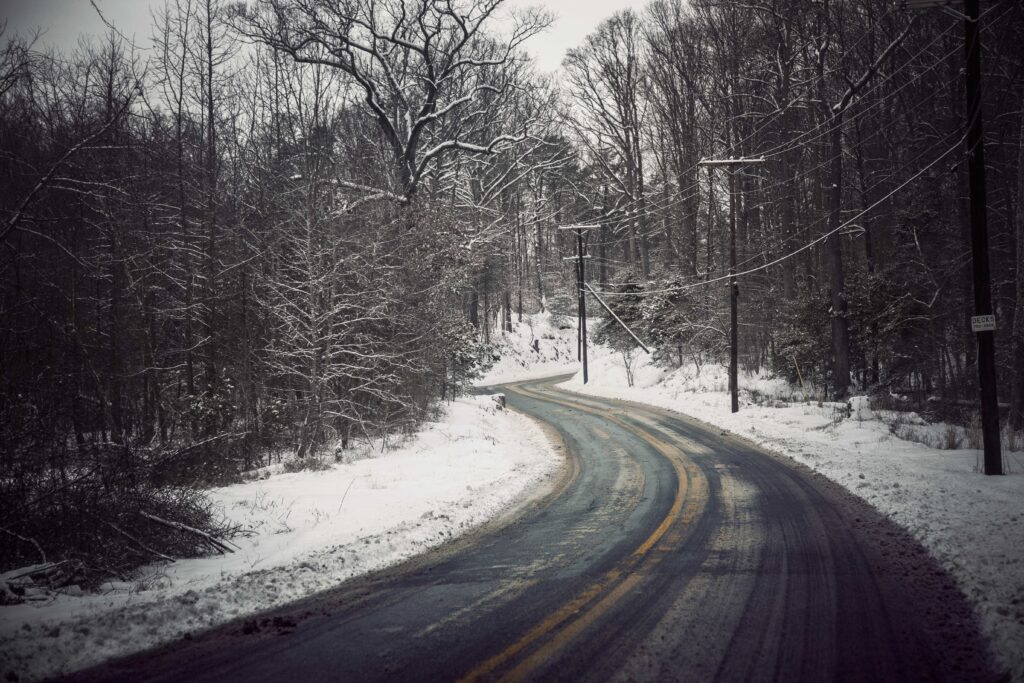 Winding snowy road through bare trees in serene winter forest with soft overcast lighting Wallpaper