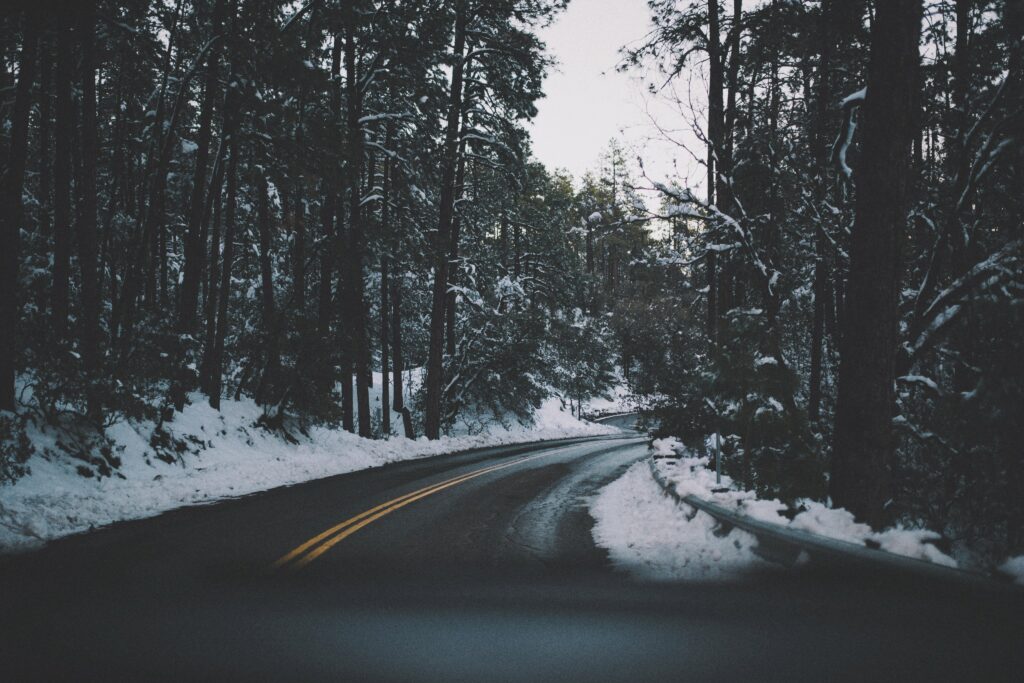 Winding asphalt road through snowy forest with tall trees and soft white snowbanks winter landscape Wallpaper