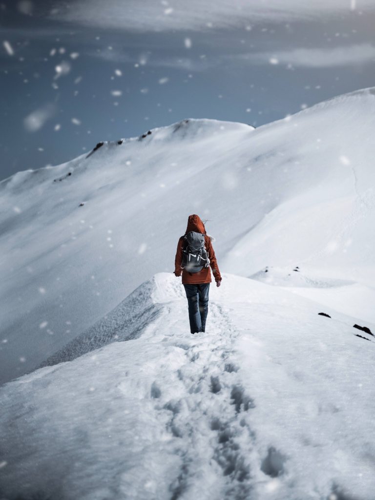 Lone hiker in orange jacket trekking snowy mountain ridge winter adventure 4K travel wallpaper