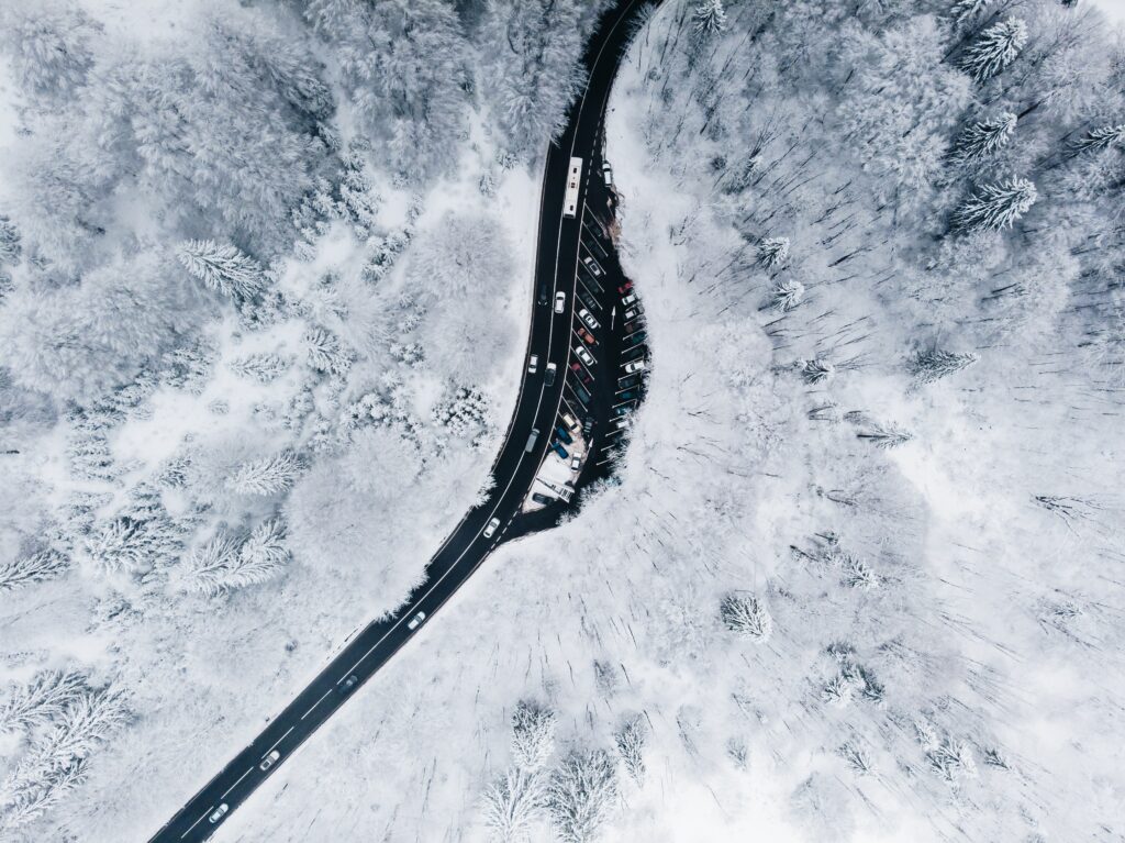 Aerial view of winding road through snow-covered forest with frosted trees and parked cars Wallpaper