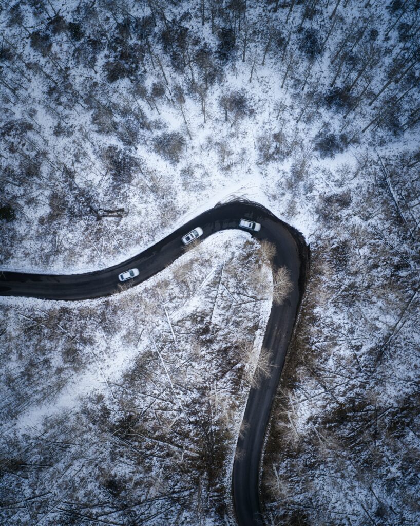 Aerial view of winding road with cars through snowy forest winter landscape wallpaper background