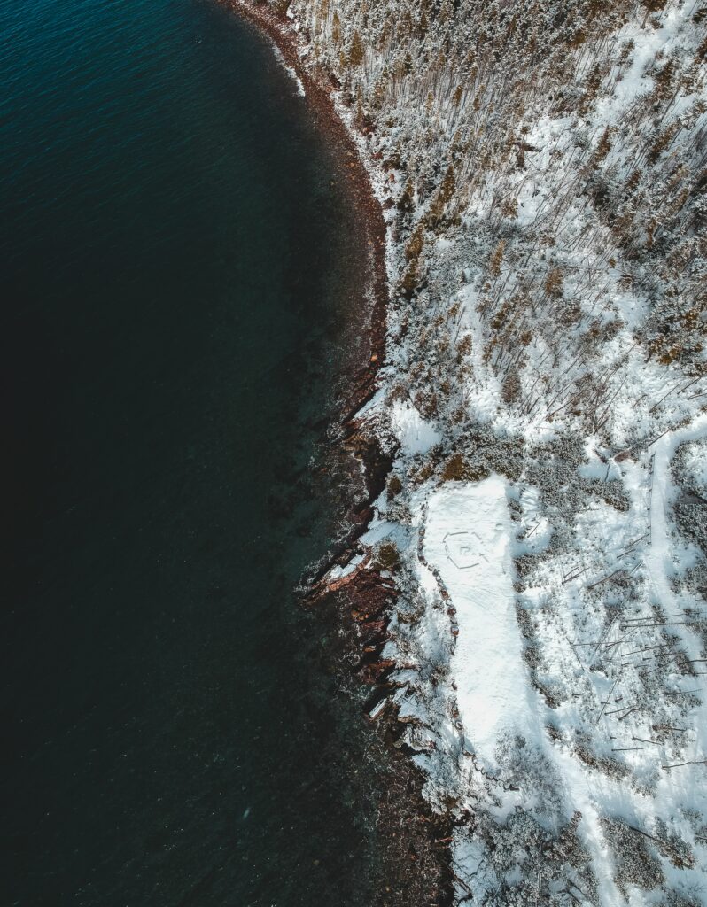 Aerial view of rugged coastline with deep blue sea meeting snow-covered shore winter landscape Wallpaper