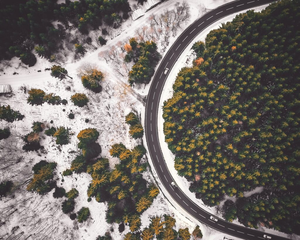 Aerial view of winding road through snow-covered dense forest with dark green treetops winter scene Wallpaper