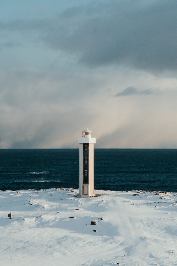 Solitary lighthouse on snowy coast overlooking dark blue sea under cloudy winter sky wallpaper