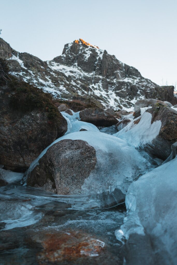 Frozen rugged stones with frosty ice and snow-dusted mountain under clear blue winter sky Wallpaper