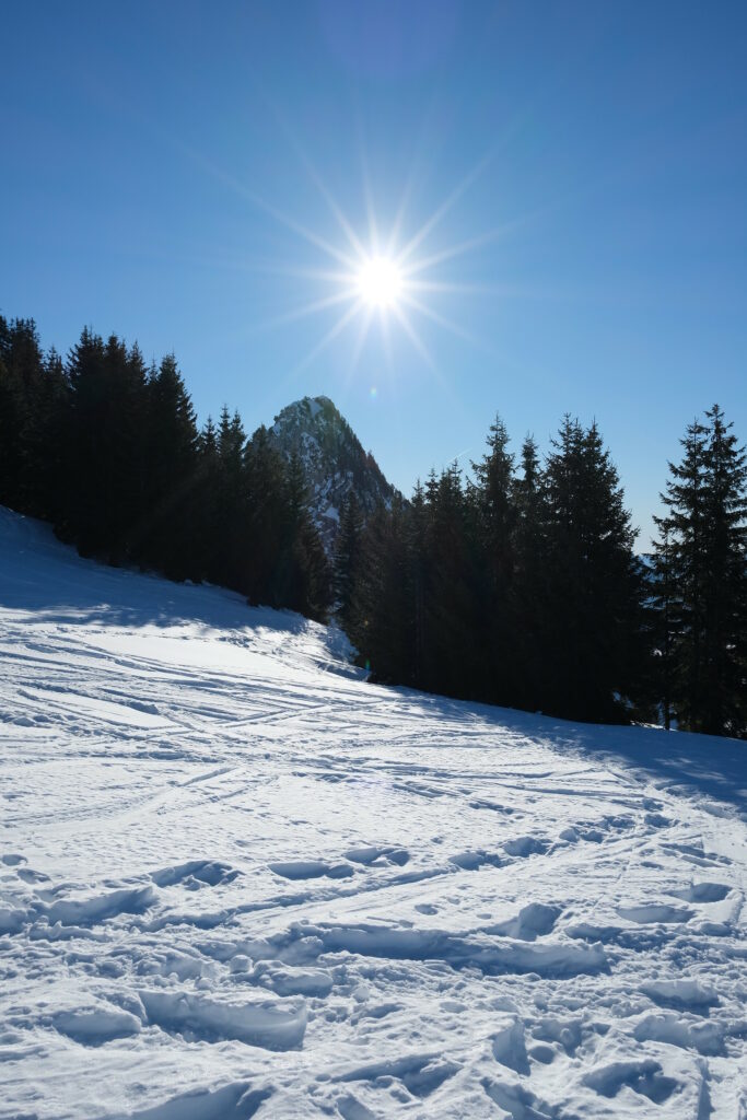 Winter wallpaper with sun rays over snow-covered mountains and evergreen trees under blue sky