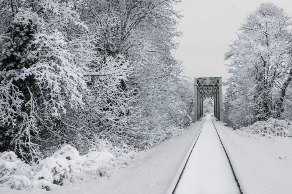 Winter railway scene with snow-covered trees and steel bridge under overcast sky background Wallpaper