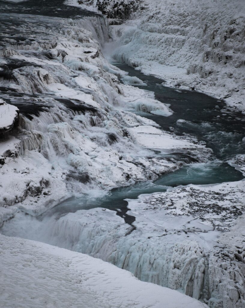 Winter river flowing through rugged icy rocks with snow layers in a serene blue landscape Wallpaper