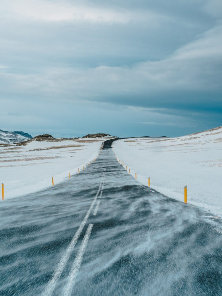 Solitary road through snow-covered fields with yellow markers under a cloudy winter sky Wallpaper
