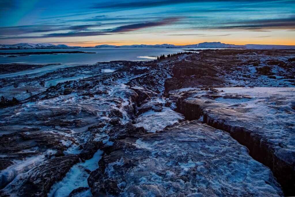 Snow-covered rocky terrain and textured stones under a dramatic winter sky with distant mountains Wallpaper