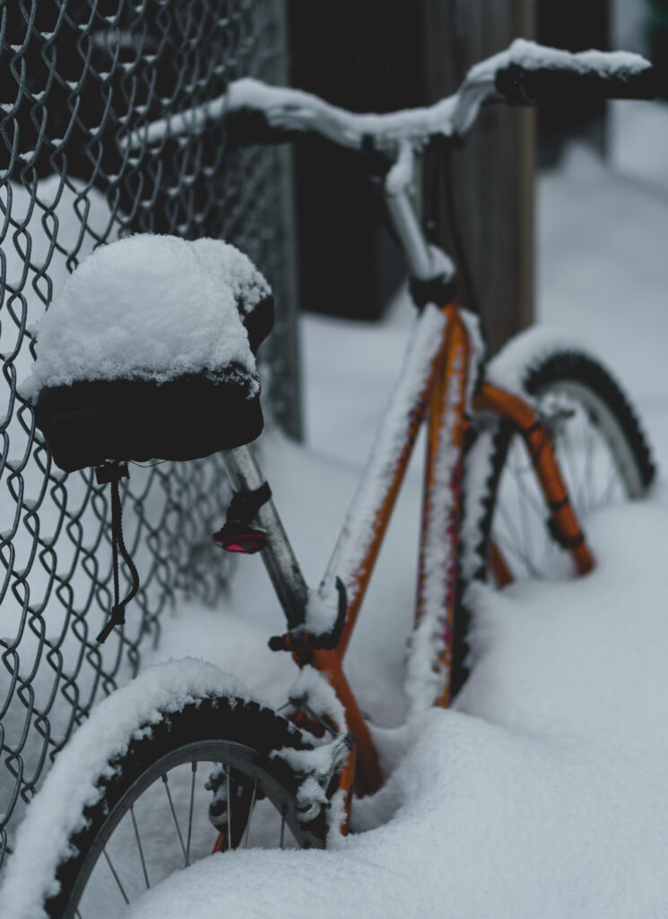 Red bike covered in fresh white snow leaning on chain-link fence serene winter scene wallpaper