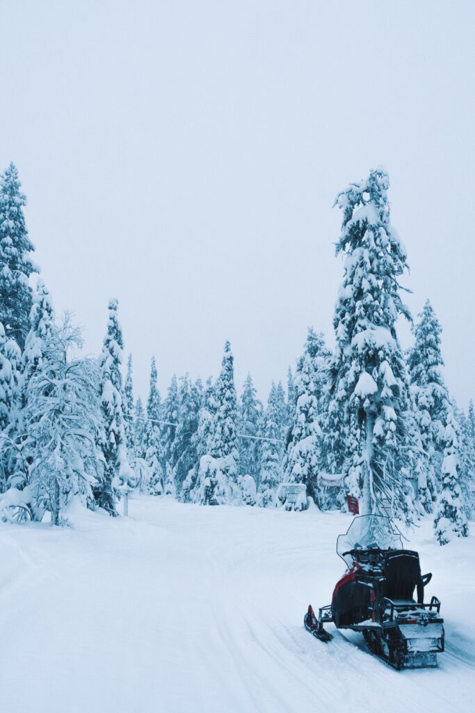 Snowmobile parked on snowy trail amid dense snow-covered trees in peaceful winter forest scene Wallpaper