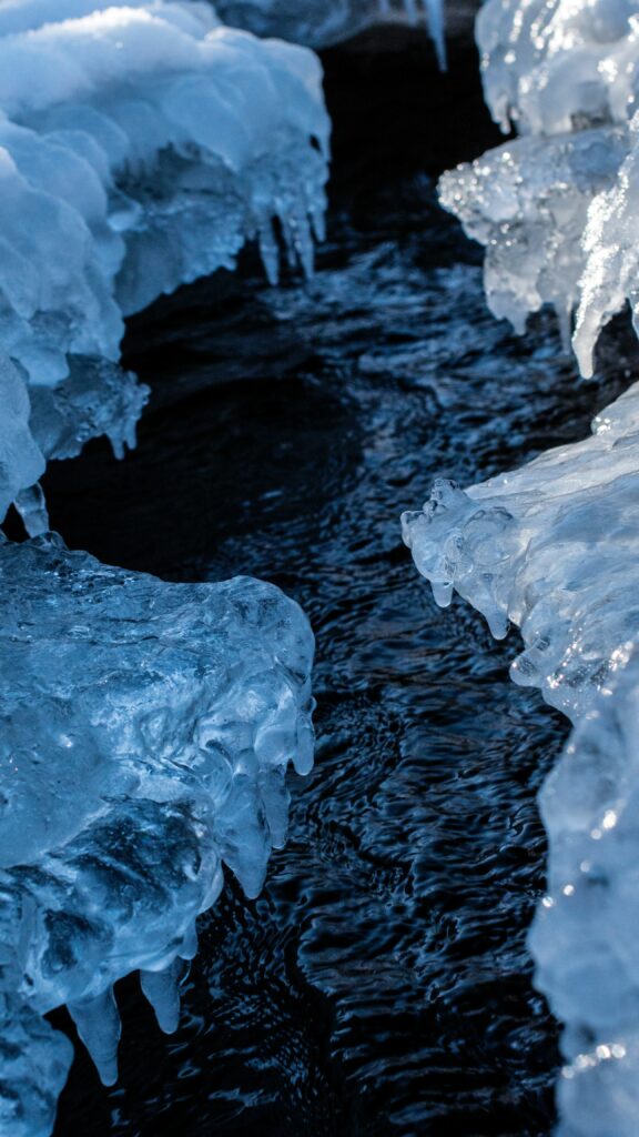 Icy blue formations along flowing stream winter wallpaper background showcasing natural tranquility