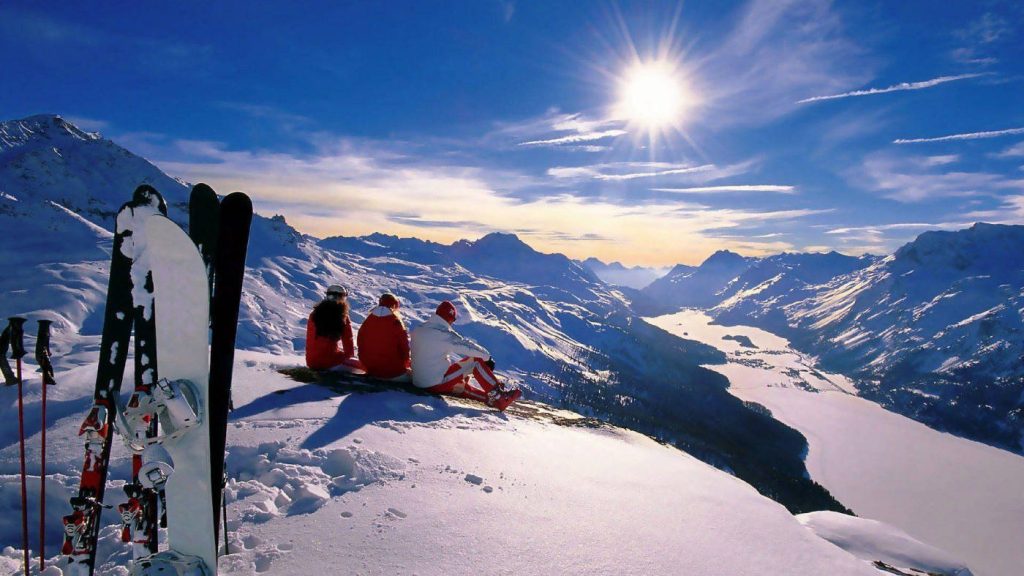 Three skiers on snowy ridge at golden winter sunrise with alpine peaks and valley view wallpaper