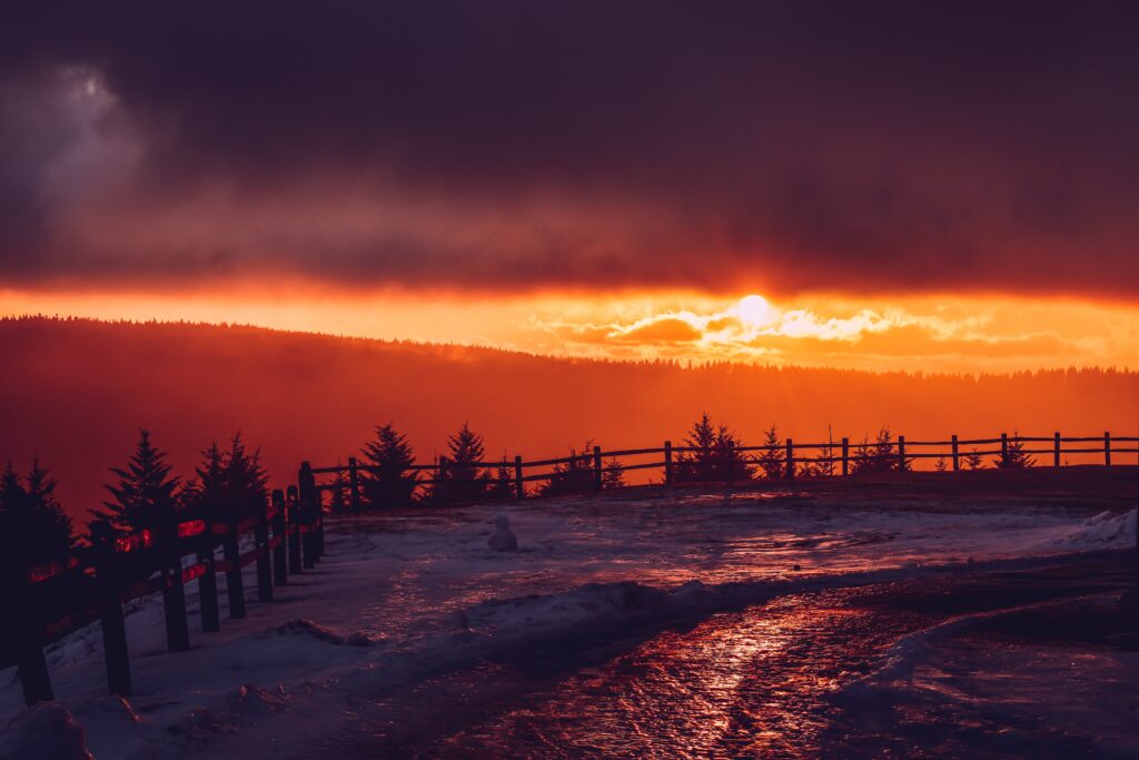 Winter sunset over snowy mountains with wooden fence and silhouetted trees serene landscape Wallpaper