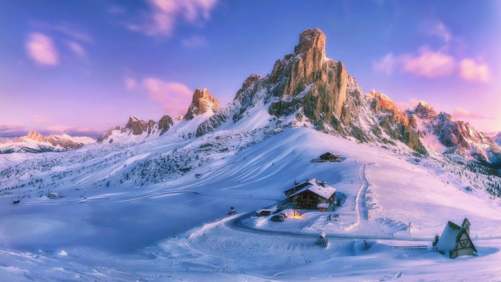 Winter sunset over snow-dusted Ra Gusela peak Dolomites with alpine refuge and stone chapel Wallpaper