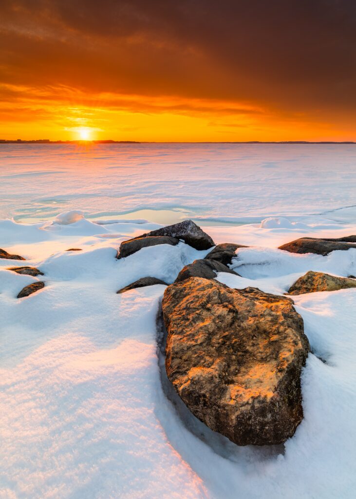 Snow-covered rocks at sunset with warm orange light and vibrant winter sky background wallpaper