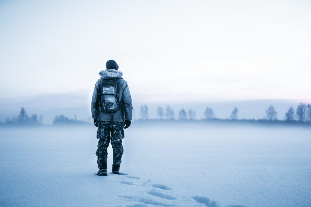 Man with backpack stands in snowy winter landscape gazing over misty frozen field wilderness adventure Wallpaper