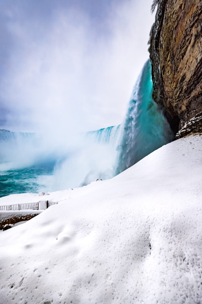 Majestic waterfall beside rocky cliff with snow and turquoise water in winter landscape wallpaper