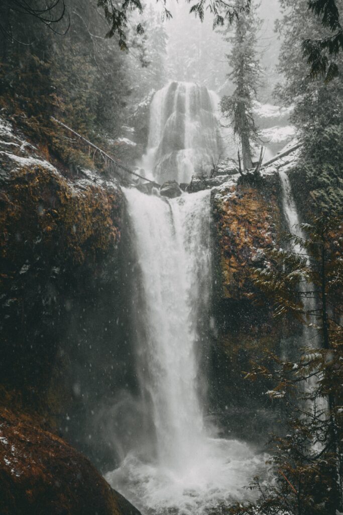 Winter waterfall cascading rugged cliff snow-dusted trees misty icy serene nature wallpaper