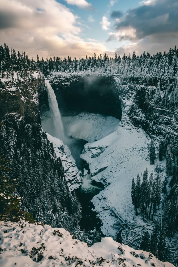 Winter landscape wallpaper with snow-covered pine trees and waterfall cascading over rugged cliff