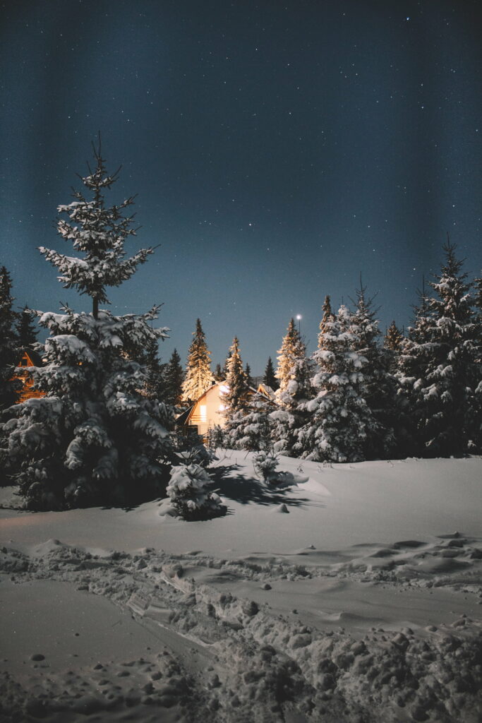 Winter Magic: A Cozy Cottage Beneath the Starry Cold Night Sky in the Snowy Mountains Wallpaper