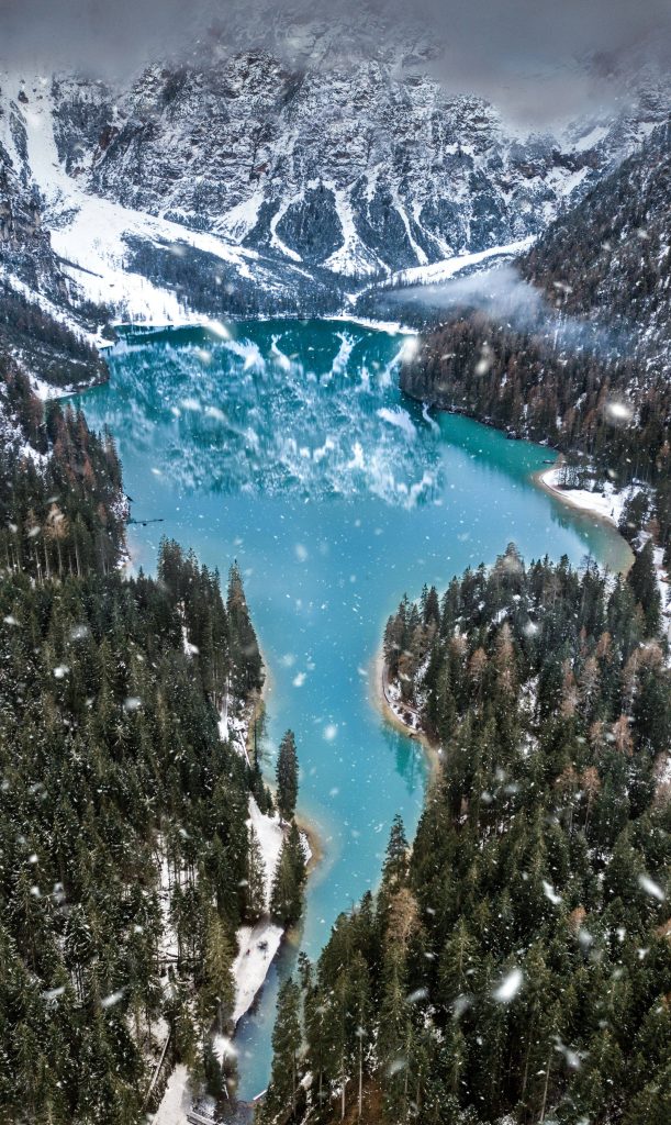 Aerial view of Lago di Braies turquoise lake surrounded by snowy Dolomite peaks and evergreen forests Wallpaper
