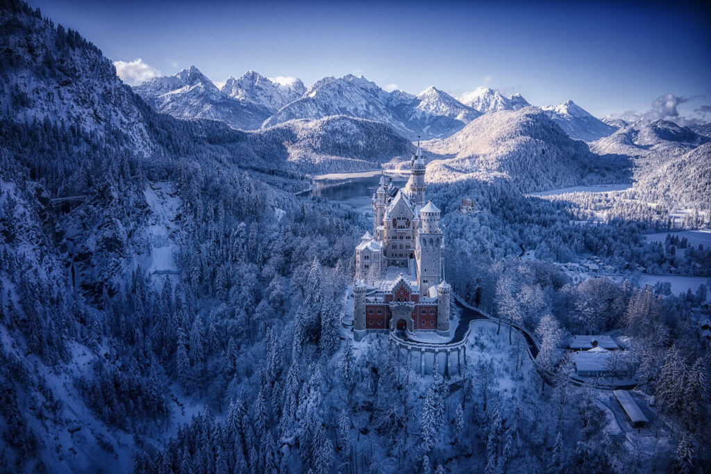 Winter Wonderland: Neuschwanstein Castle Blanketed in Snow amidst Enchanting Forest Wallpaper